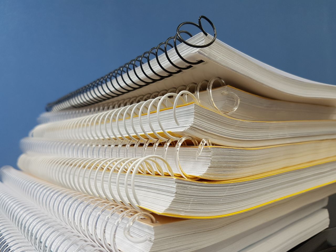 Close-up of stacked spiral notebooks with varied bindings against a blue backdrop.